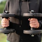 Close-up of a woman holding dumbbells outdoors, focusing on fitness and strength training.