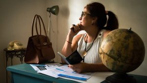 Businesswoman pondering at her desk with a globe, documents, and a lamp. Captures intellectual ambiance.